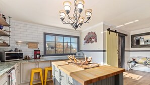 Una cocina moderna con una isla central, taburetes amarillos, una araña y un ventanal grande.