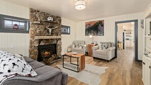 Un salón acogedor con chimenea de piedra, sillones a rayas y un sofá gris.