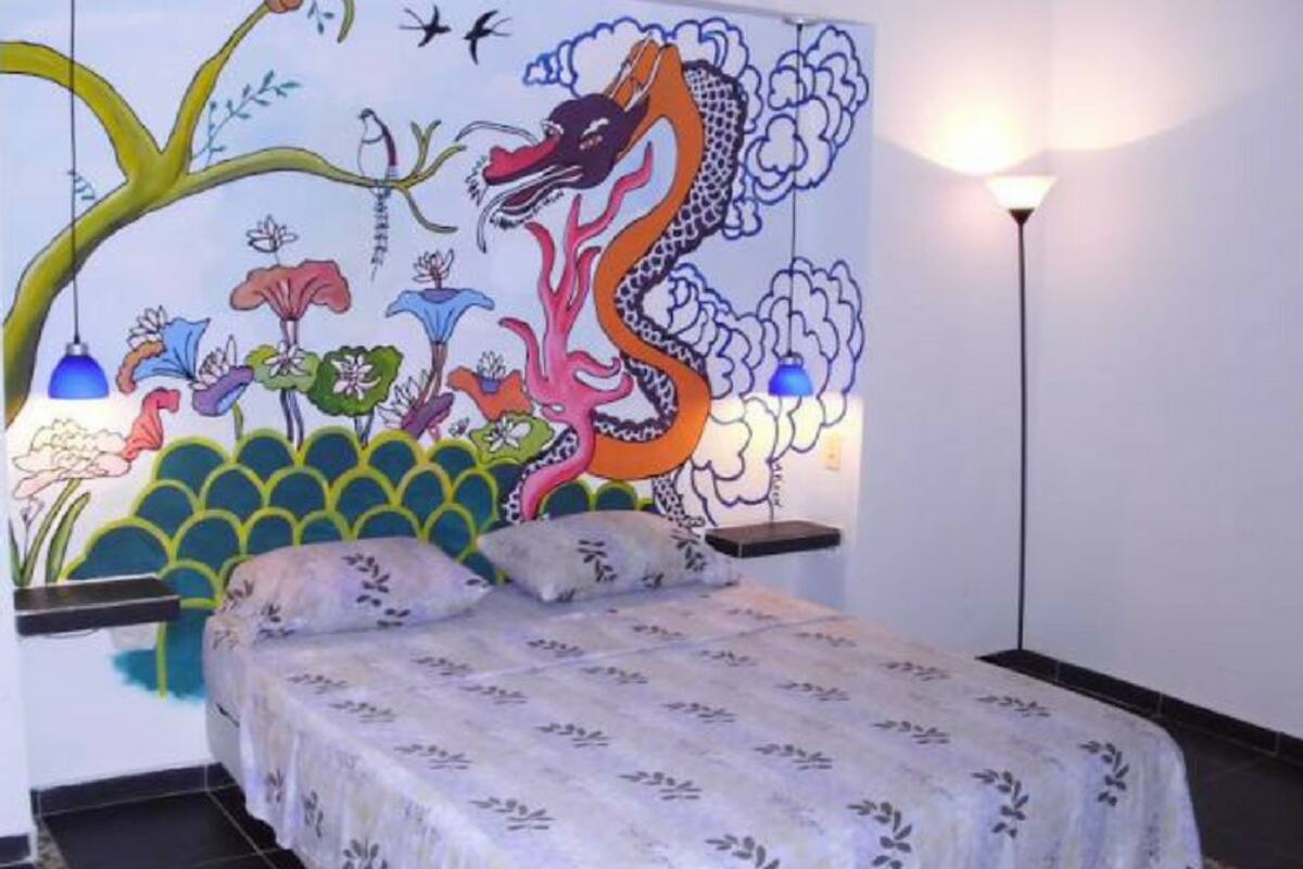 Un dormitorio con un mural colorido en la pared, una cama con colcha estampada y una lámpara de pie.