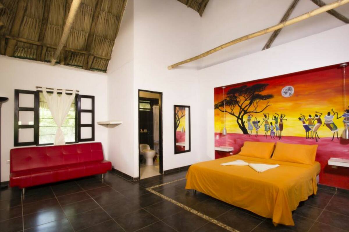 Una habitación con una cama, un sofá rojo, un cuadro y una ventana con cortinas.