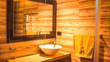 Un baño con pared de madera, un espejo grande, un lavabo y una toalla colgada en un perchero.