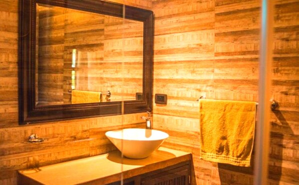 Un baño con pared de madera, un espejo grande, un lavabo y una toalla colgada en un perchero.