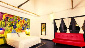 Una habitación con una cama, un sofá rojo, un mural colorido y un cuadro en la pared.