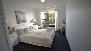 A bedroom with a bed, bedside tables, a desk, a chair, and a view of the outdoors.