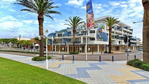 A modern hotel with a multi-story structure, a flag, and palm trees. - Blue Coral Terrace, Coast Apartment 31 (The Entrance)