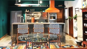 A modern kitchen with a central island, a dining area with patterned chairs, and a colorful rug. - Pipa Casa Mandacarú (Tibau do Sul)