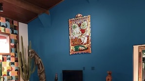 A living room with a blue wall, a wooden TV stand, a cactus, and a colorful geometric floor pattern. - Pipa Casa Mandacarú (Tibau do Sul)