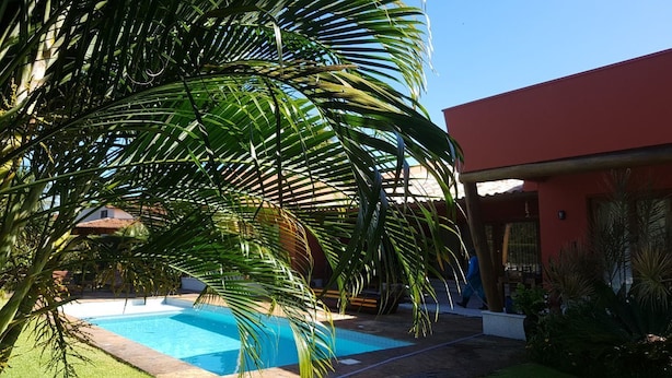 A swimming pool surrounded by lush greenery and a red building. - Pipa Casa Mandacarú (Tibau do Sul)