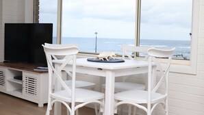 Un comedor amplio con una mesa, sillas, un televisor de pantalla plana y vistas al océano.