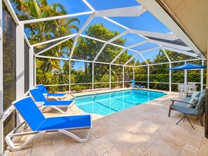 A covered outdoor swimming pool with lounge chairs and a table.