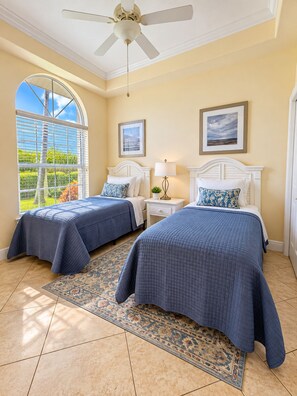 A room with two beds, a ceiling fan, a large window with blinds, and a rug.