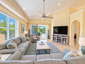 A spacious living room with a sofa set, a coffee table, a TV on a wooden stand, and a ceiling fan.