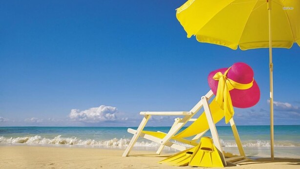 Ein Strandstuhl und ein Sonnenschirm am sandigen Strand mit dem Meer im Hintergrund.