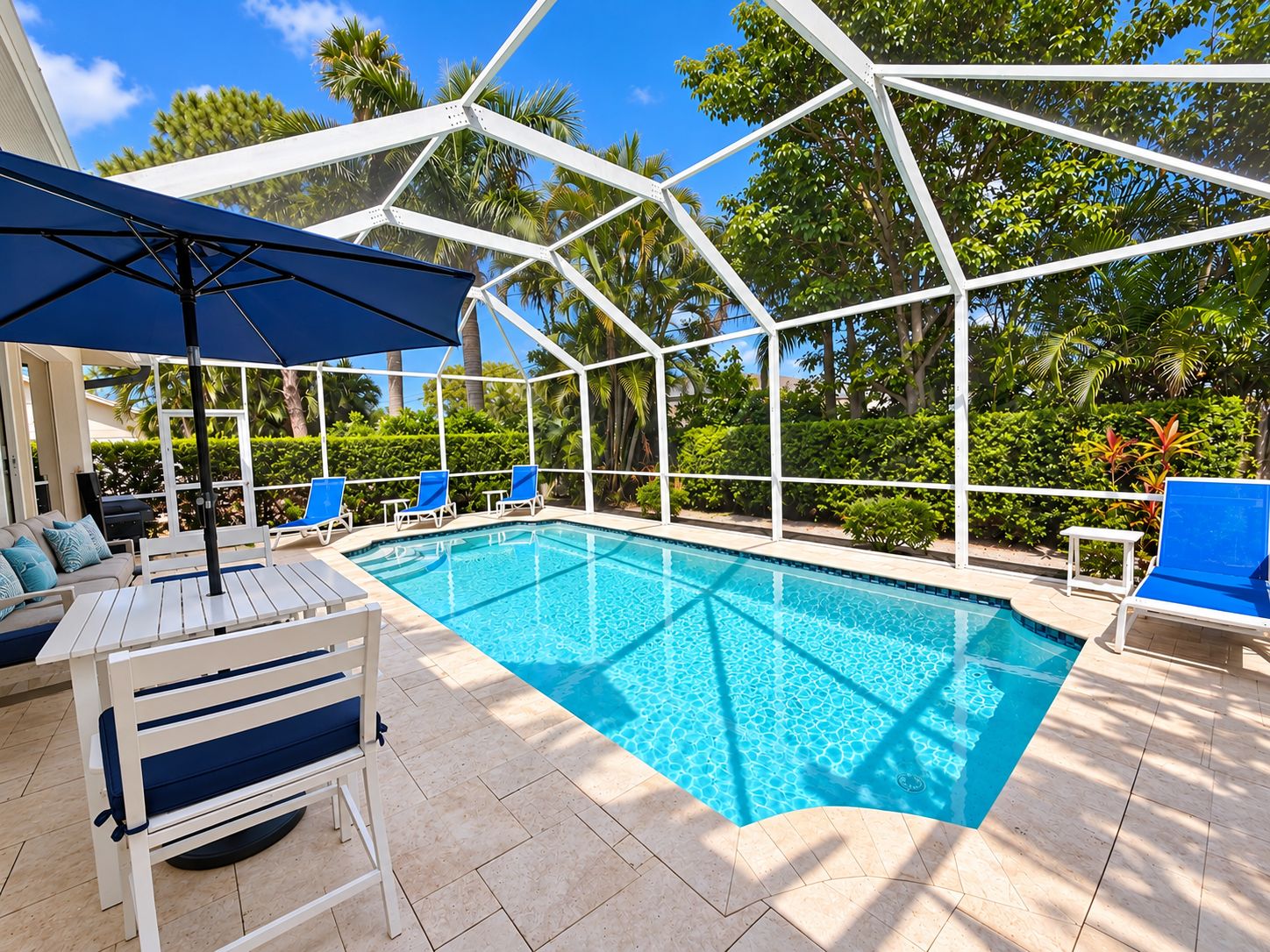 A pool area with a clear blue pool, white lounge chairs, and a covered seating area with a table and chairs.