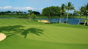 Ein Golfplatz mit Sandbunkern, Palmen und einem Wasserspiegel.