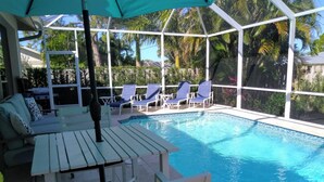 Ein Poolbereich mit überdachtem Sitzplatz, Liegestühlen und einem Tisch.