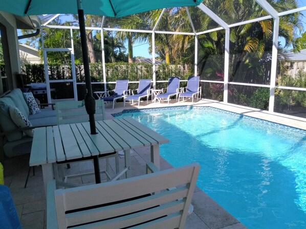 A pool area with a covered seating area, lounge chairs, and a table. - High End 4 Bdrm Heated Pool Walk To Gulf Walk To Mercato Walk To The Ritz (Naples)