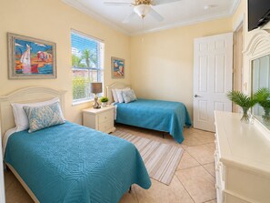 A bedroom with two beds, a nightstand, a lamp, and a window with blinds.