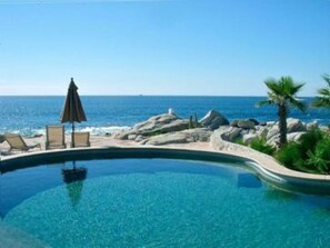 A pool with a view of the ocean, surrounded by rocks and palm trees.