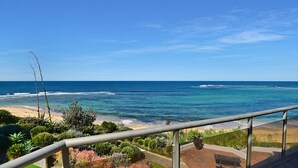 Un balcon avec vue sur l’océan, une plage de sable et diverses plantes.