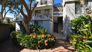 Un bâtiment moderne doté d’un balcon, d’un arbre et d’un chemin menant à l’entrée.