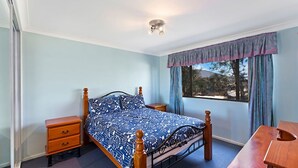 Quarto com cama, mesas de cabeceira, janela com cortinas e luminária no teto.