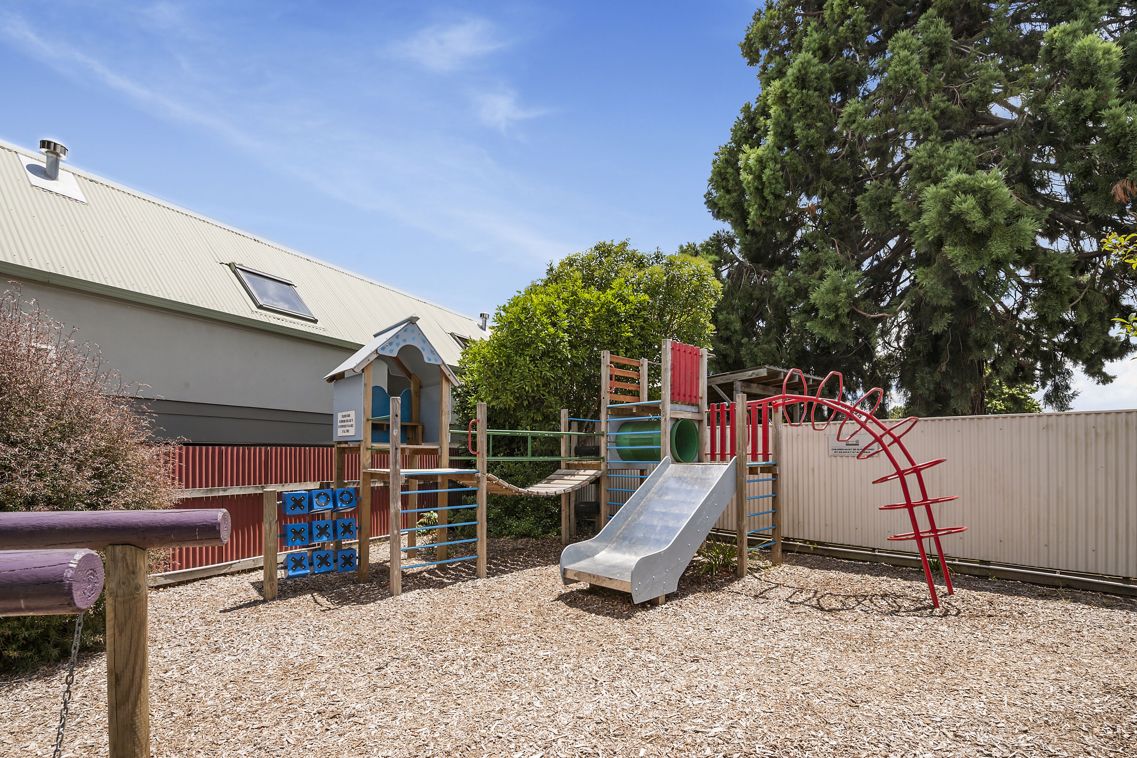 A playground with a slide, climbing structures, and a small building with a window.