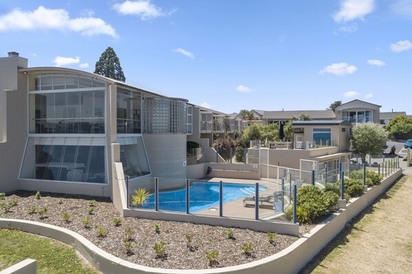 A modern residential building with a swimming pool, large windows, and a well-maintained garden. - The Village Resort (Taupo)