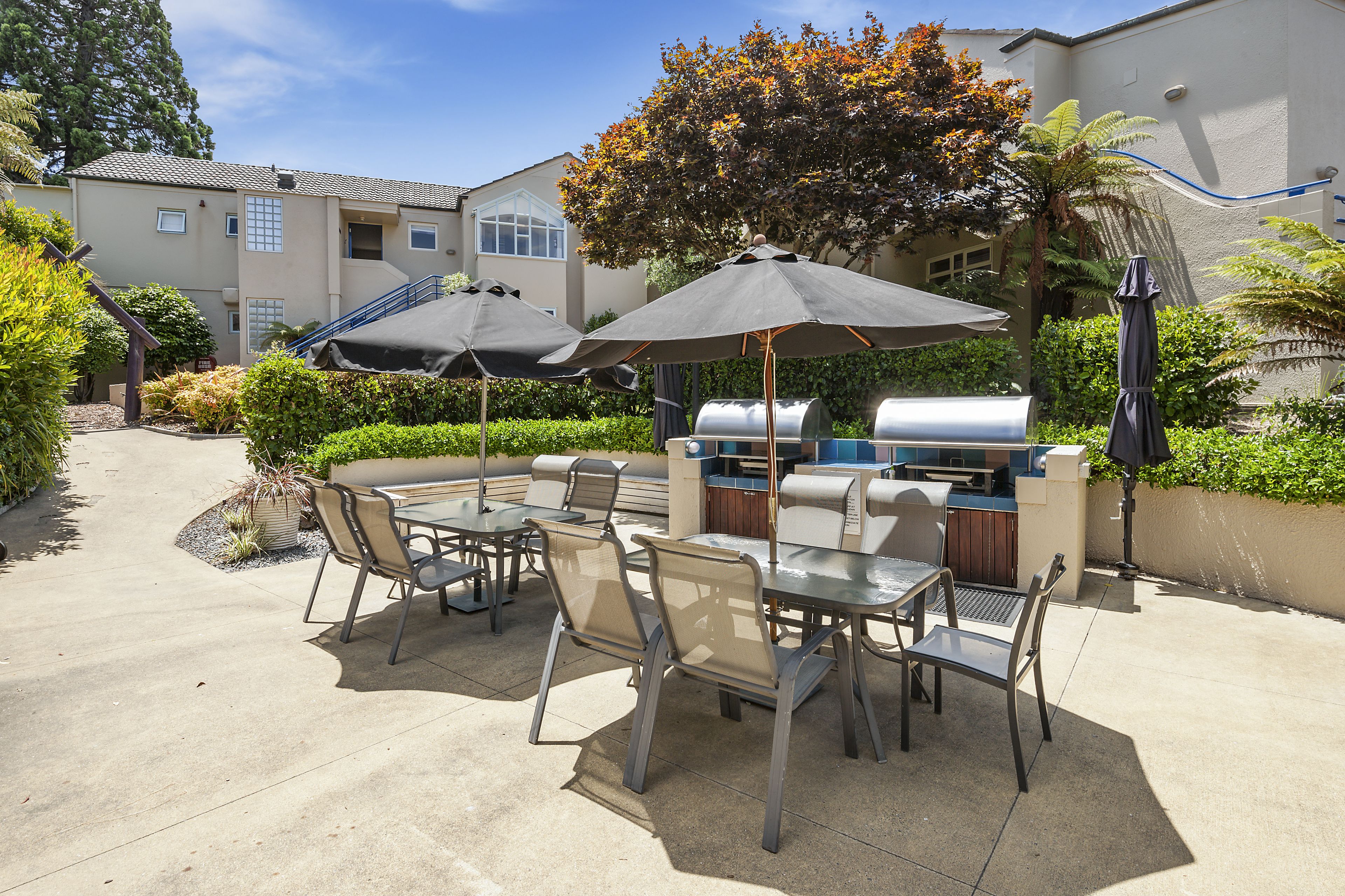 An outdoor patio with a grill, dining table, chairs, and umbrellas.