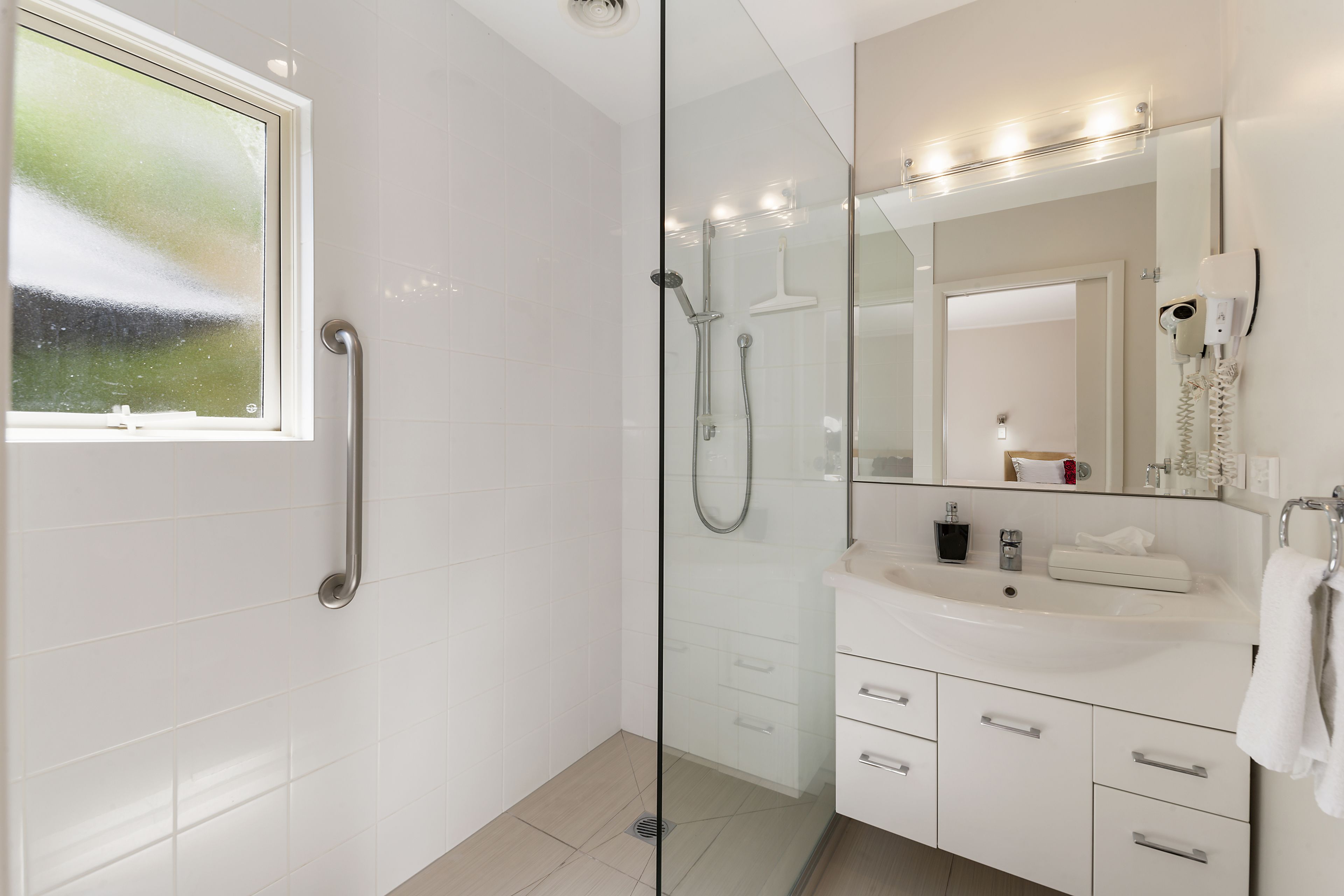 Un baño moderno con cabina de ducha de vidrio, tocador con espejo y ventana.