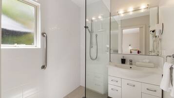 Un baño moderno con cabina de ducha de vidrio, tocador con espejo y ventana.