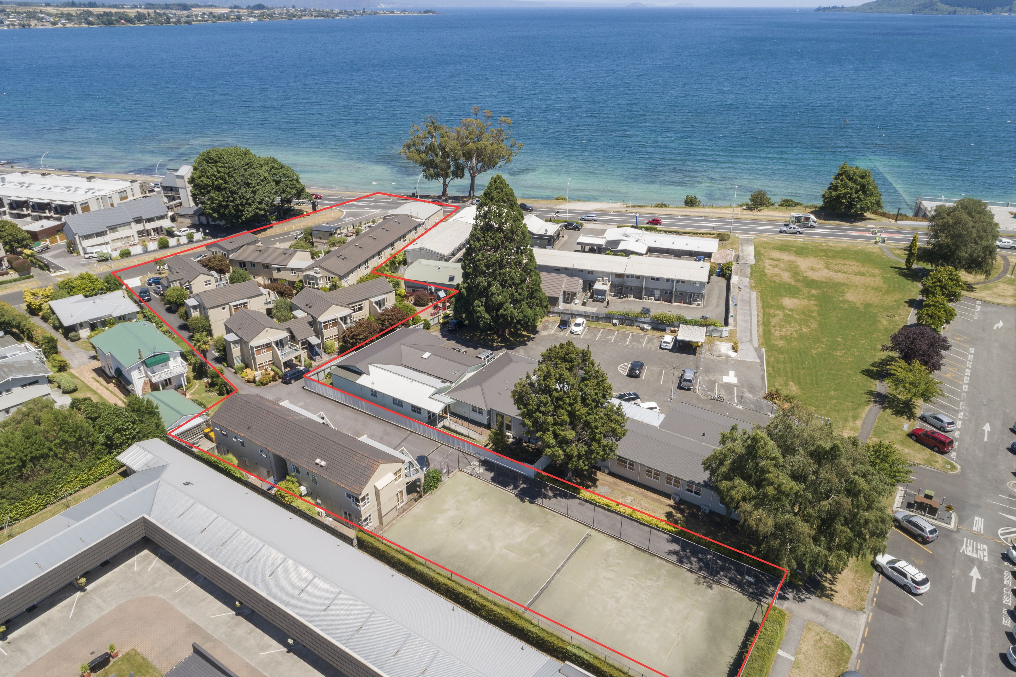 An aerial view of a residential area with houses, a parking lot, and a large body of water in the background.