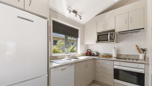 A modern kitchen with white cabinetry, a dishwasher, a microwave, and an oven. - The Village Resort (Taupo)