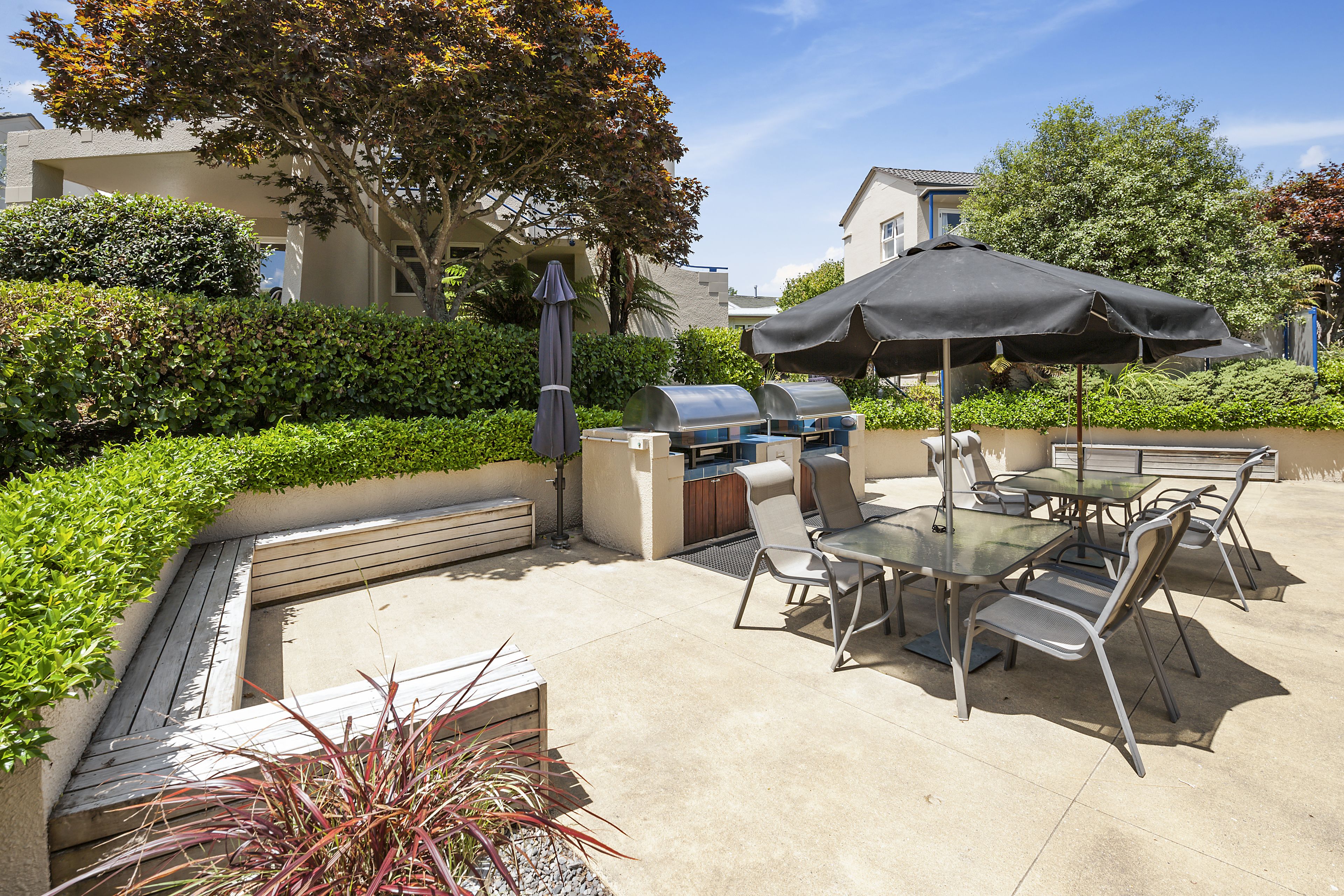 Eine Terrassenanlage im Freien mit Grill, Esstisch, Stühlen und Sonnenschirm.