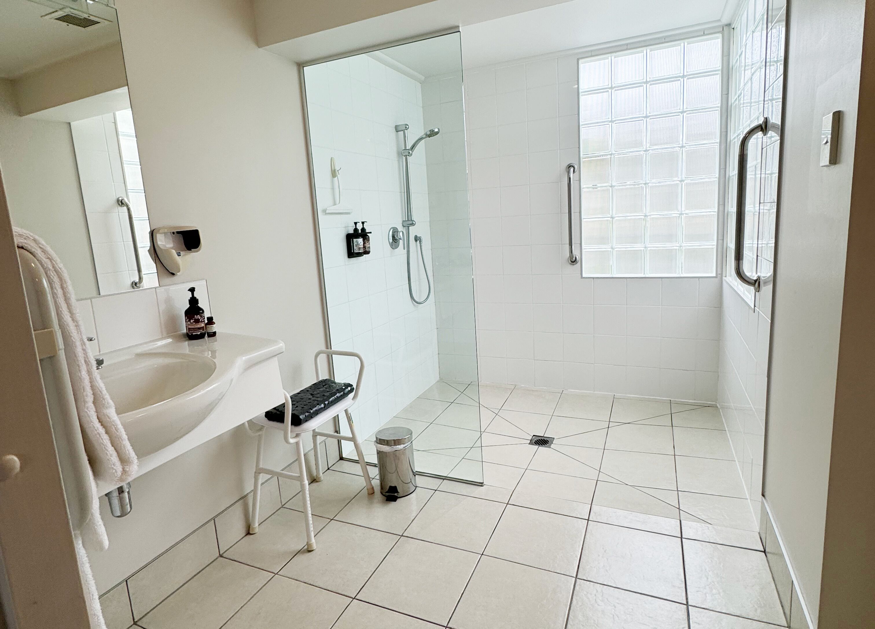 Un baño moderno con un lavamanos blanco, cabina de ducha de vidrio y ventana que deja entrar luz natural.