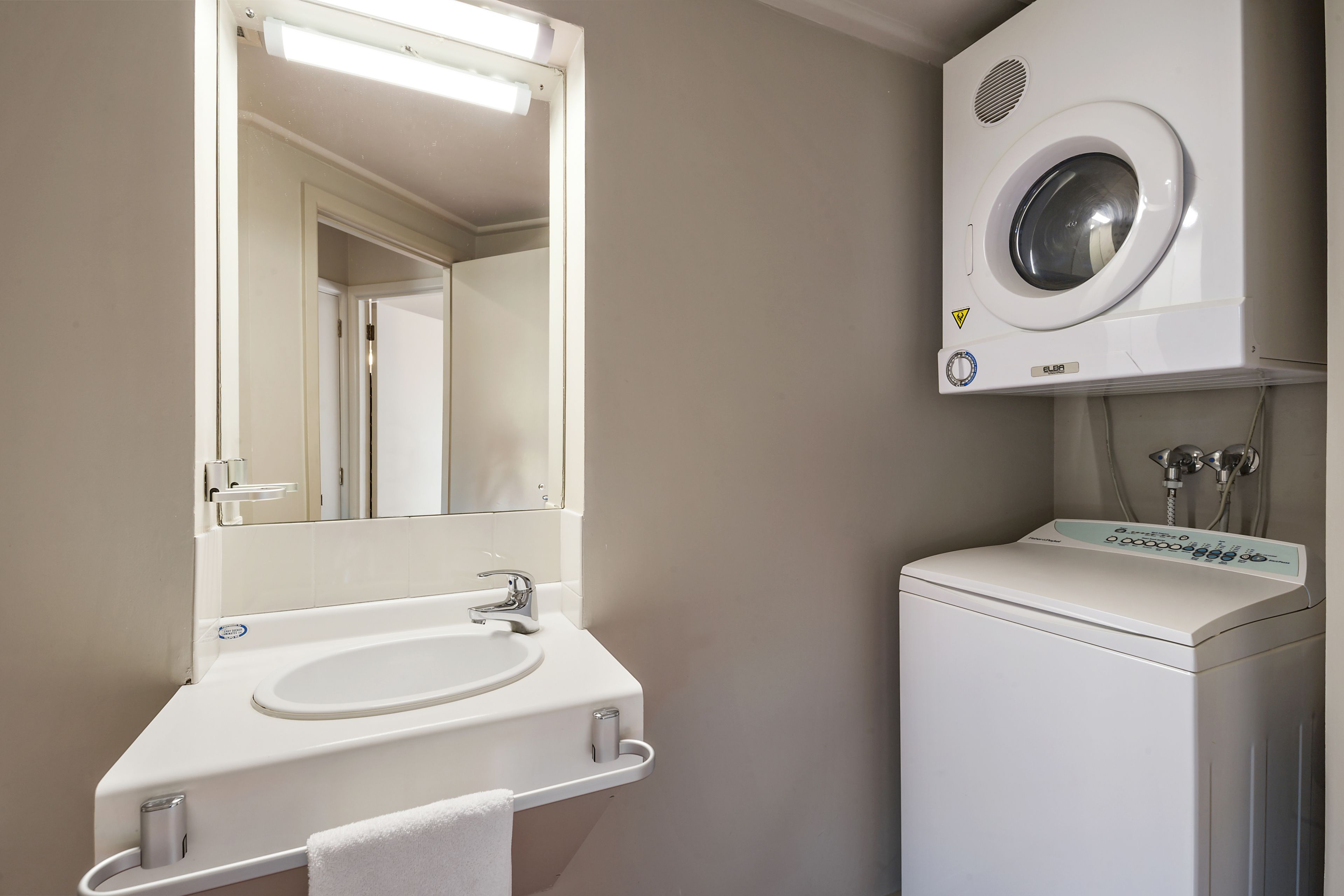 A bathroom with a sink, mirror, and a front-loading washing machine.