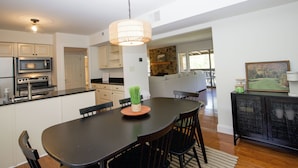 A modern kitchen with a central island, a dining area with a black table and chairs, and a living area with a sofa and a coffee table.