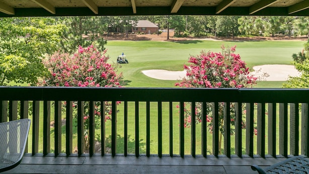 A view from a covered porch overlooking a golf course with a house in the background.