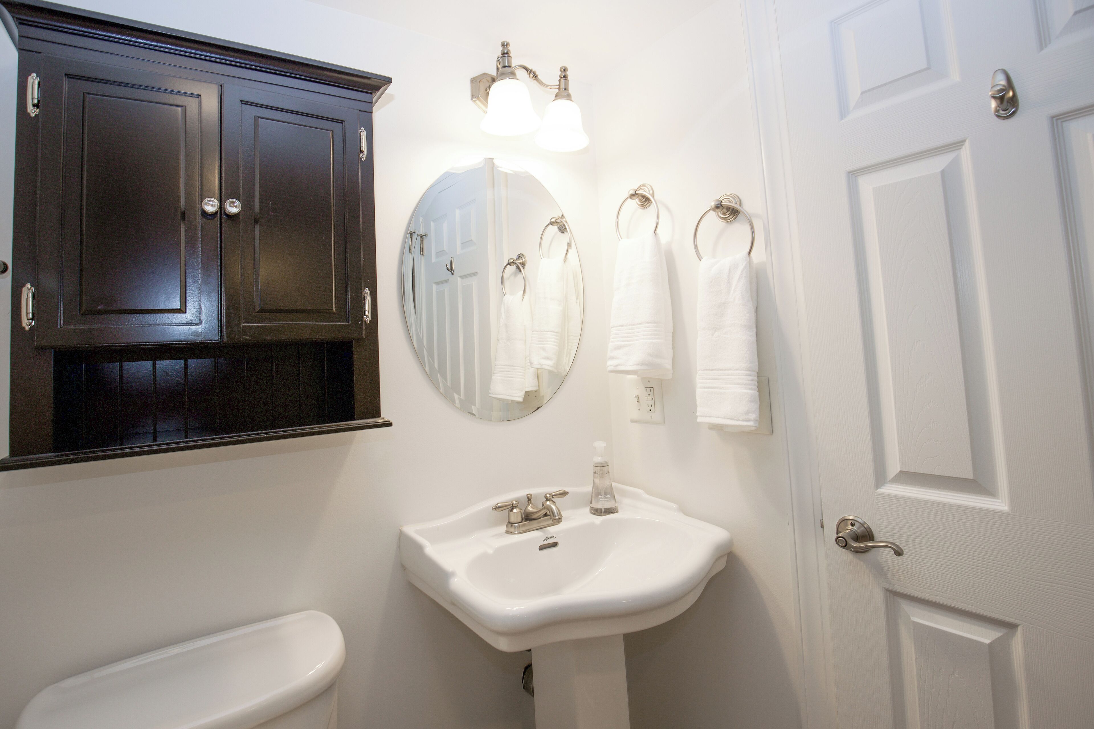 Une salle de bain avec un lavabo blanc, des meubles sombres, un miroir et une porte.