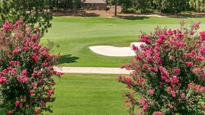 A golf course with a sand bunker, surrounded by trees and a building in the background.