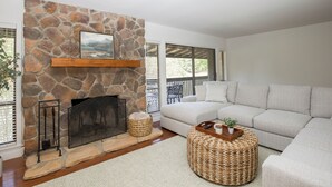 A living room with a stone fireplace, a white sofa, and a wicker ottoman.