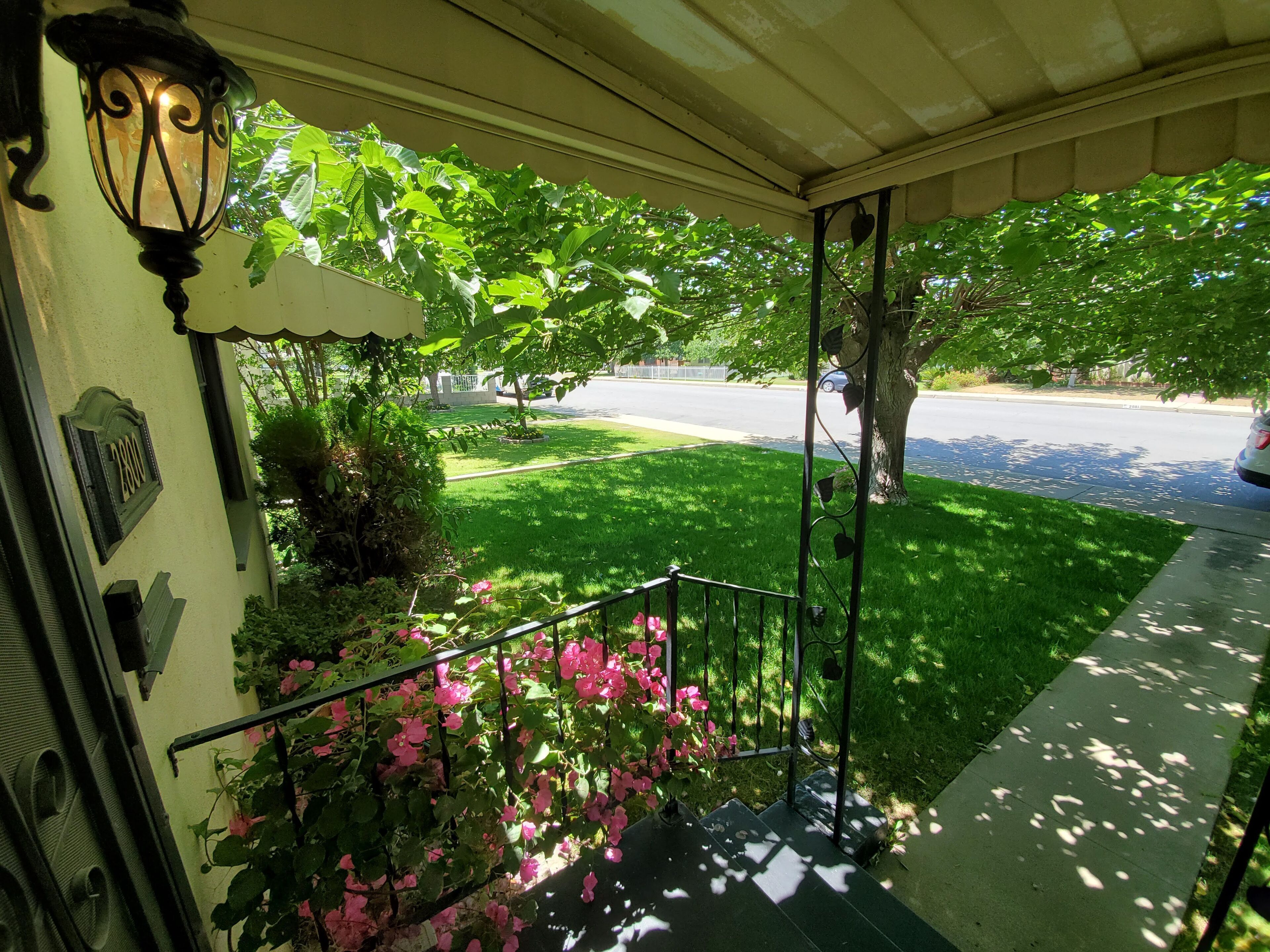 A front porch with a green lawn, a metal railing, and a street view.