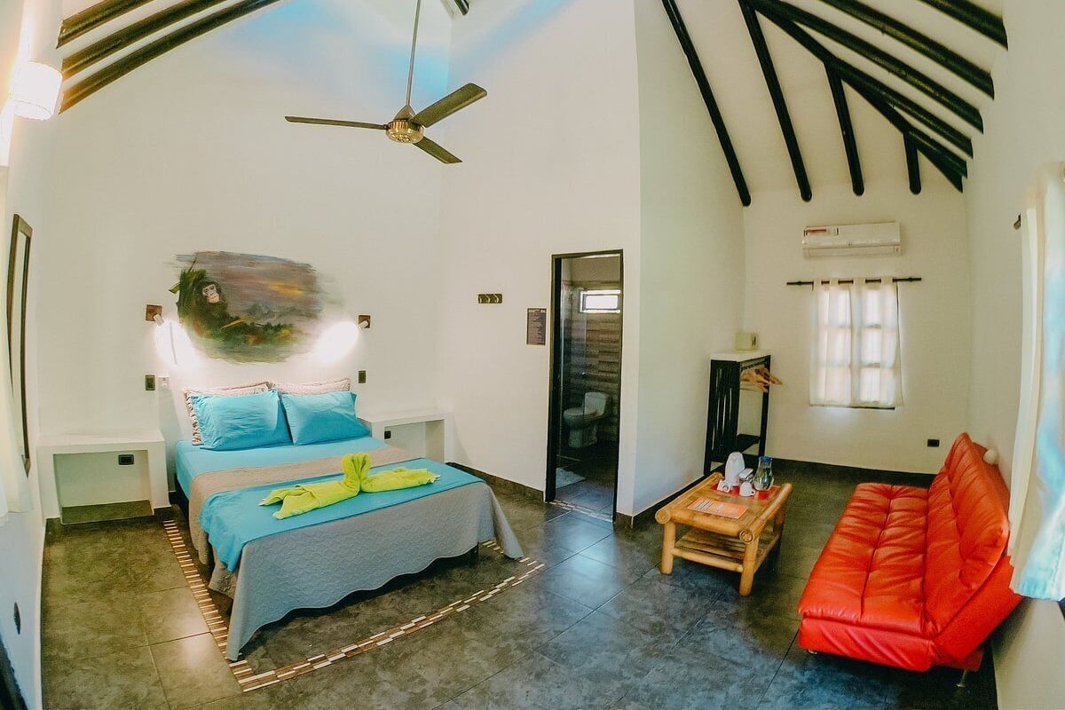 A bedroom with a bed, a red sofa, a wooden table, and a ceiling fan.
