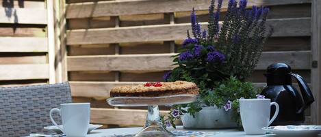 A round table with a glass cake stand, two white cups, a coffee pot, and a floral tablecloth.