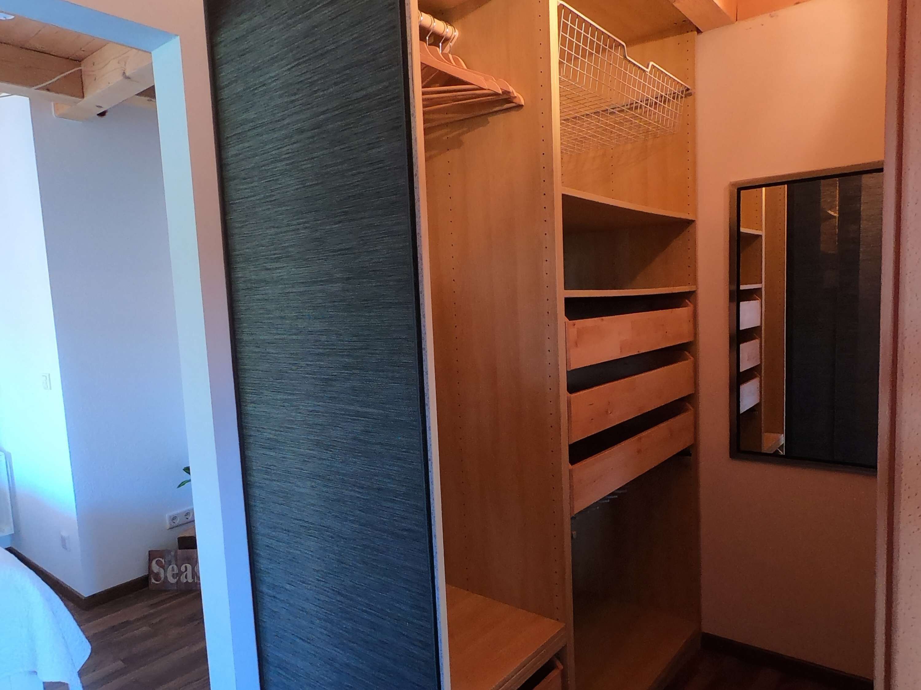 Ein begehbarer Kleiderschrank mit offenen Regalen und einer spiegelnden Schiebetür.