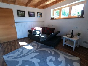 A cozy living room with a sofa, a small table with a bottle, and a window with plants.