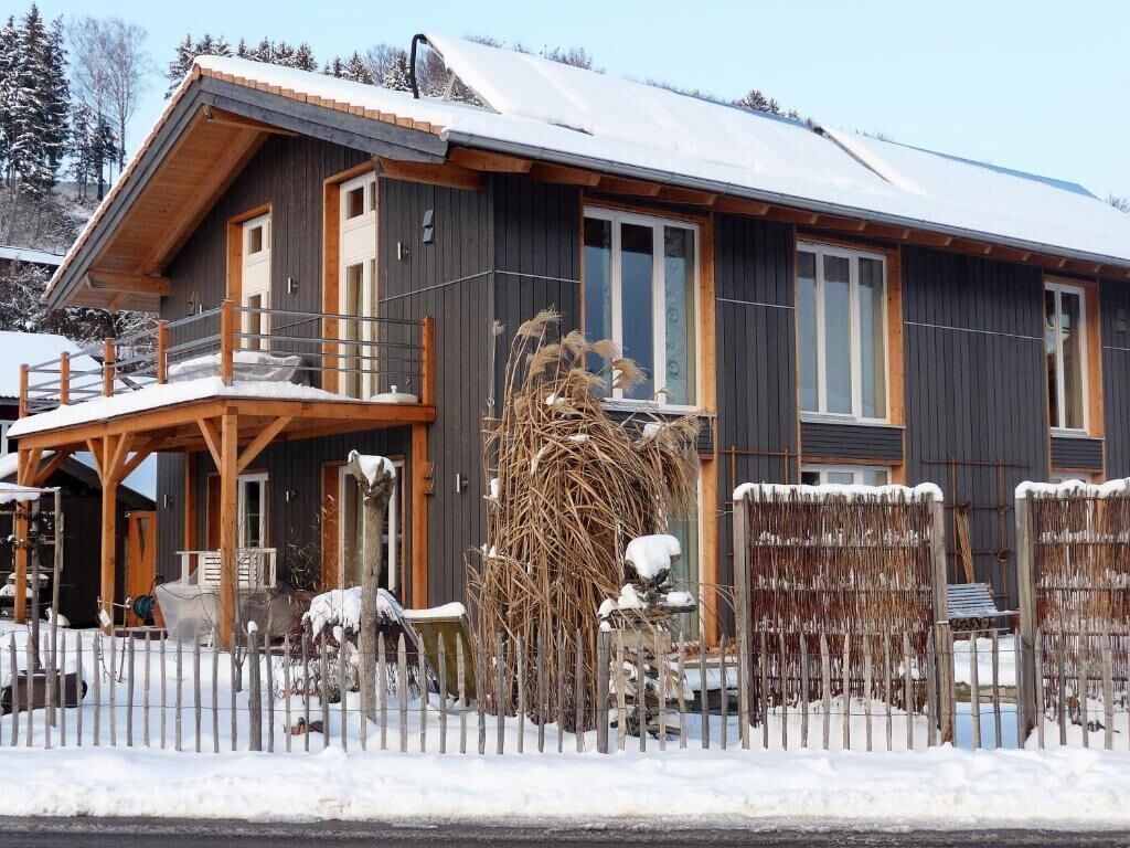 A wooden cabin with a balcony, large windows, and a snow-covered roof.