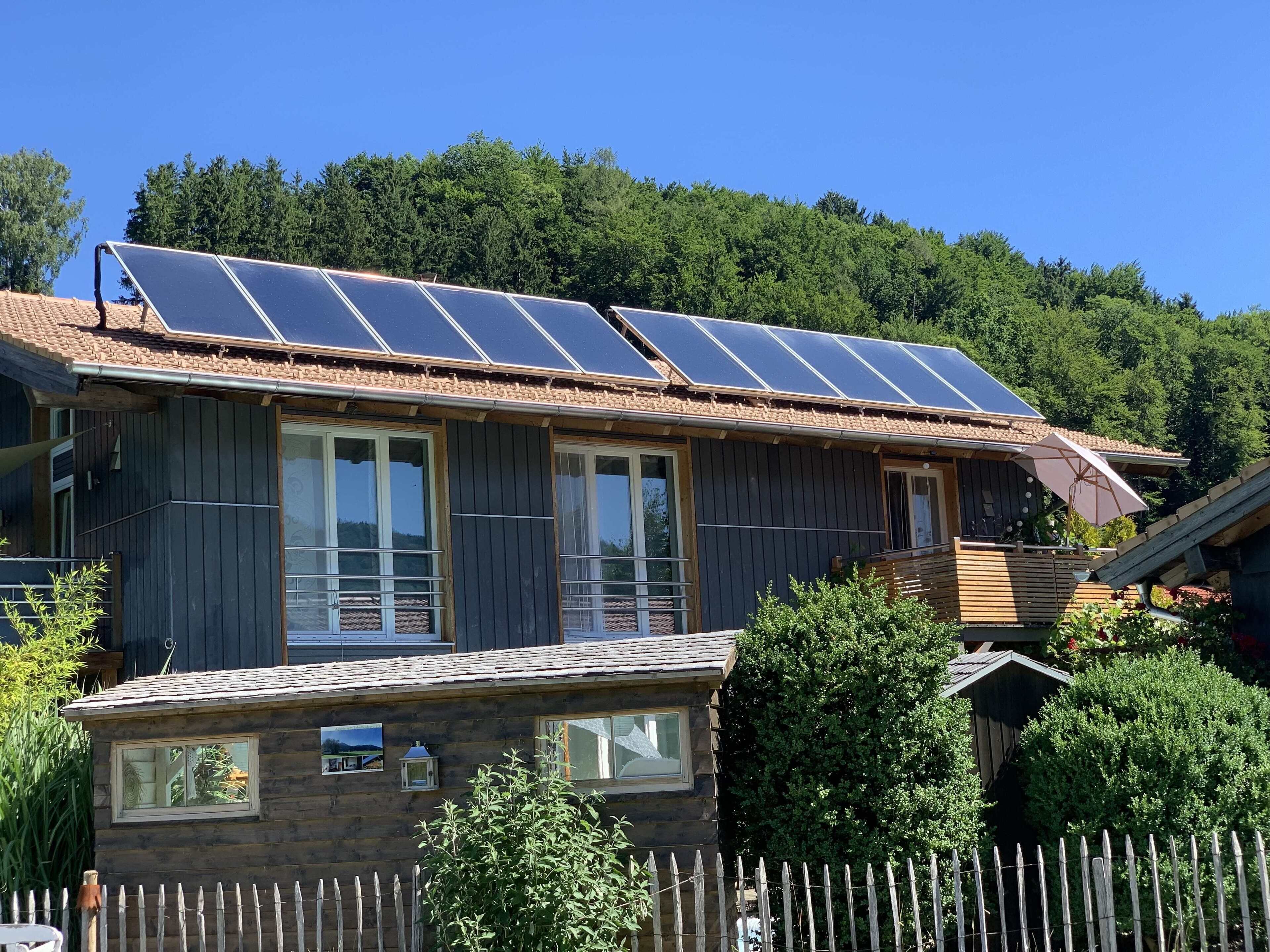 A wooden house with a sloped roof, large windows, and solar panels on the roof.