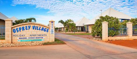 A sign for Osprey Village Holiday Apartments with a clear sky and a paved entrance.