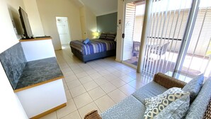 Quarto de hotel com cama, sofá, televisão e porta de vidro deslizante para o exterior.